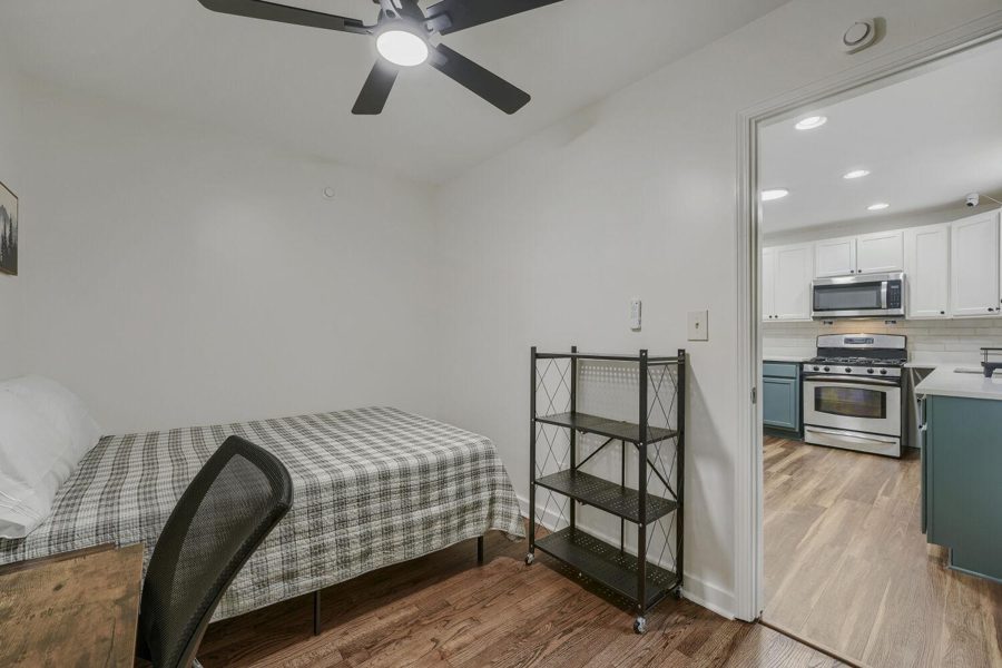 Furnished bedroom with a bed and shelving, kitchen through the door, at The Mora House